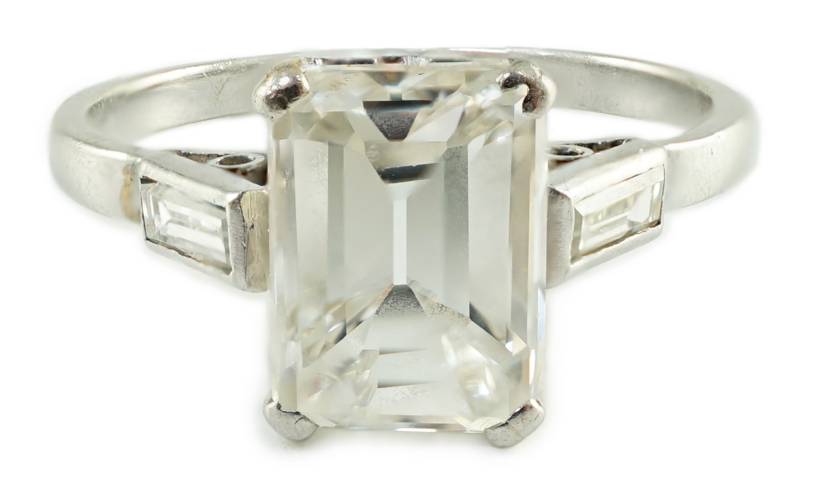 A platinum and single stone emerald cut diamond set ring, with baguette cut diamond set shoulders